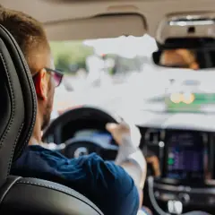 Mężczyzna za kierownicą, zastanawia się, czy przy zmianie biegów puszcza się gaz. Widok zza fotela pasażera.