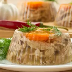 Gotowany schab w galarecie, ozdobiony marchewką i koperkiem, prezentuje się apetycznie na talerzu.