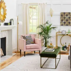 A living room with a pink armchair, gold accents, and a fan pattern artwork, showcasing what is art deco style with its geometric shapes and luxurious feel.