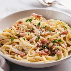 Un plat de pâtes à la carbonara crémeuses, garni de lardons, de parmesan râpé et de persil frais. Un délice italien.