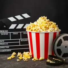 Klapka filmowa, kubełek popcornu i rolka taśmy filmowej na ciemnym tle.