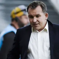 Żyżyński dziennikarz sportowy w garniturze, z uwagą obserwuje wydarzenia na boisku.
