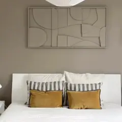Une chambre moderne avec un lit blanc, des coussins moutarde et un tableau abstrait. Une belle idée tableau créatif pour une décoration murale apaisante.