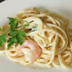 Cremige Pasta al Limone mit Garnelen und Petersilie auf einem weißen Teller. Ein Genuss für Augen und Gaumen.