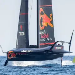 Wyścigowy jacht klasy AC75 z logo Red Bull Racing i Alinghi, unoszący się nad wodą na foilach.