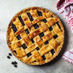 Złocista tarta z borówkami, z kratką z ciasta i kilkoma owocami obok. Idealna na letni deser.