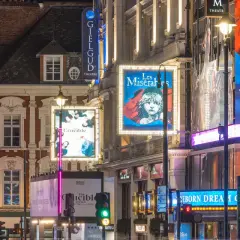 Nocne światła teatrów w londyńskim **West Endzie**: plakaty "Les Misérables", "The Crucible" i "2:22 A Ghost Story" oświetlają ulicę.