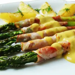 Zielone szparagi owinięte w szynkę parmeńską, polane sosem holenderskim, z ziemniakami.