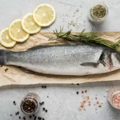 Lubina fresca, lista para cocinar. Un manjar de los pescados de temporada Galicia, acompañada de limón, romero y especias.