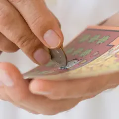 Dłoń zdrapuje monetą zdrapkę z symbolem dolara.
