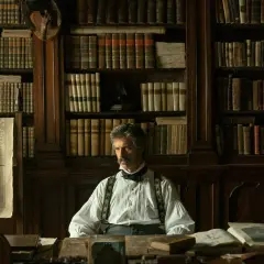 Mężczyzna w historycznym stroju siedzi w gabinecie pełnym książek, które mogą posłużyć jako inspiracja do seriali na podstawie książek.
