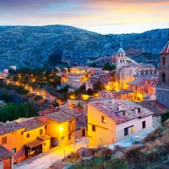 Pueblo español iluminado al anochecer, ideal para escapadas fin de semana España. Casas con tejados de teja y torres de iglesias se alzan entre colinas.