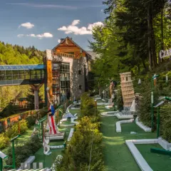 Mini golf z atrakcjami jak Krzywa Wieża w Pizie i Statua Wolności, obok budynku i lasu.