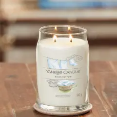 Zapalone świece zapachowe Yankee Candle Clean Cotton w szklanym słoju na drewnianym stole.