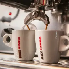 Två vita kaffekoppar fylls med italienskt kaffe från en espressomaskin.