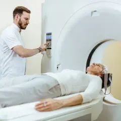 Pacjentka leży na stole tomografu, technik przygotowuje badanie. Czy można pić wodę przed tomografią z kontrastem? Zapytaj lekarza.
