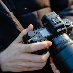 Dłonie trzymają aparat Nikon Z6 III z obiektywem.