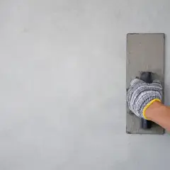 Mano con guanto che esegue la rasatura di un muro con una cazzuola.