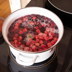Gotuje się kompot z wiśni w białym garnku na płycie indukcyjnej. Owocowy napój pachnie latem.