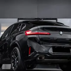 Elegancki, czarny BMW X4 G02 z przyciemnianymi szybami i sportowymi felgami prezentuje się imponująco na tle nowoczesnej, szarej ściany.