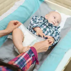 Mama zmienia pieluszkę maluszkowi. Dobór odpowiednich rozmiarów pampersów jest kluczowy dla komfortu dziecka.
