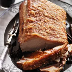 Poitrine de porc croustillante, dorée et juteuse, servie sur une assiette ornée avec des épices.