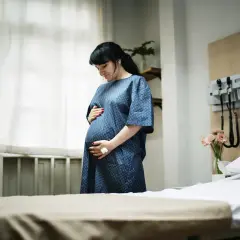 Kobieta w szpitalnej sali, trzymająca się za brzuch, szuka sposobów, jak złagodzić skurcze porodowe.