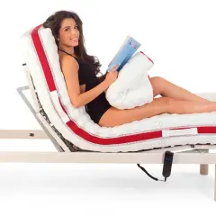 Donna sorridente legge un libro a letto, con il materasso regolabile che offre la postura corretta per guardare la TV o rilassarsi.