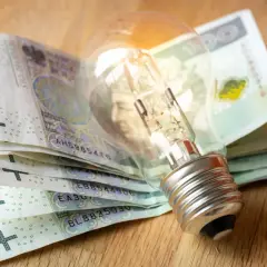 Żarówka na stosie banknotów 100 zł. Symbolizuje wysokie rachunki za prąd i potrzebę oszczędzania.