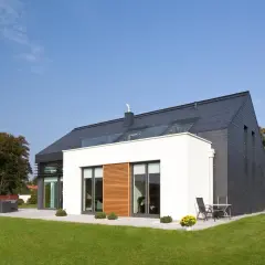 Nowoczesny dom z białym tynkiem na elewacji i ciemnym dachem. Wokół zadbany ogród.