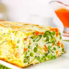 Un delicioso pastel de verduras, con guisantes, zanahoria y calabacín, horneado en un molde rectangular.