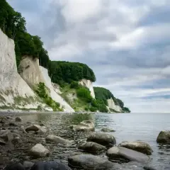 Majestatyczne, białe klify Rugii wznoszą się nad kamienistą plażą i spokojnym morzem.