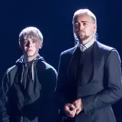 Scorpius Malfoy w czarnej bluzie obok starszego mężczyzny w eleganckim stroju.