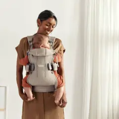 Uśmiechnięta mama tuli dziecko w nosidełku Babybjorn. Od kiedy można używać? Od pierwszych dni życia!