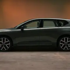 Volvo EX60 gris oscuro, perfil lateral, con fondo degradado naranja y suelo de hormigón.