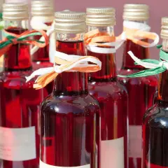 Rzędy butelek z rubinowym winem z rabarbaru, ozdobione kolorowymi wstążkami.