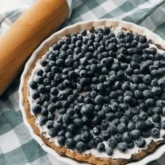 Pyszna tarta z borówkami i kremowym mascarpone, gotowa do pieczenia. Obok wałek do ciasta.
