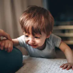 Gråtande bebis med rött hår, en high need baby som håller en vuxen hand.