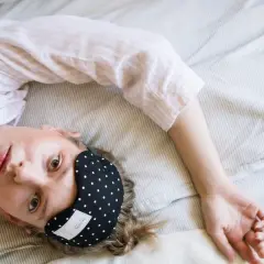 Kobieta w piżamie leży na łóżku z opaską na oczy, marząc o spokojnym śnie, jak po zażyciu zolpidemu.