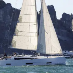 Un elegante catamarano solca acque azzurre, con vele bianche gonfie di vento, mentre sullo sfondo si stagliano scogliere rocciose.