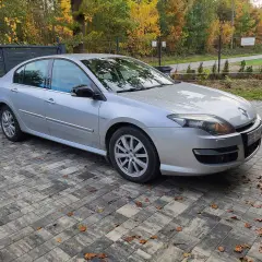 Srebrny sedan Laguna 3 2.0 dCi zaparkowany na podjeździe z kostki brukowej, otoczony jesienną roślinnością.