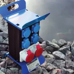 Niebieska erbetka z gniazdami elektrycznymi stoi na kamieniach obok stawu.