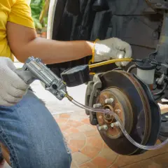 Mechanik odpowietrza hamulce, sprawdzając objawy zapowietrzenia układu. Widać narzędzie z manometrem podłączone do zacisku hamulcowego.