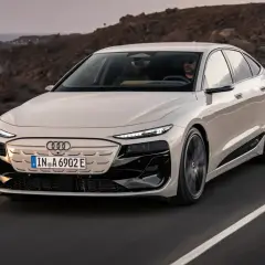 Elegancki Audi A6 e-tron w kolorze kremowym przemierza malowniczą, nadmorską drogę.