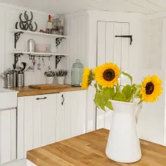 Helle Küche im modernen Landhausstil mit Spülbecken, Holzarbeitsplatte und Sonnenblumen. Offene Tür gibt Blick auf grünen Garten frei.