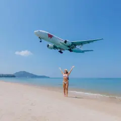 Frau am Strand jubelt, als ein Flugzeug landet. Der Traum vom Urlaub in Thailand wird mit dem Visum Thailand wahr.