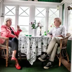 Britt Skogman och en man sitter vid ett bord i ett solrum.