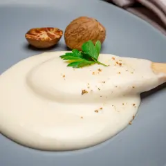 Krämig bechamelsås på en grå tallrik, med muskotnötter och persilja. Perfekt för ditt bechamelsås recept.
