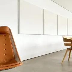 En brun läderfåtölj och en rad trästolar framför vita paneler på väggen, som hjälper till att minska eko i rummet.