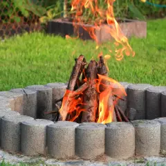 Ognisko z kostki brukowej płonie w ogrodzie, otoczone zieloną trawą.
